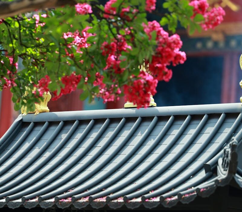 Pink flowers contrast beautifully against a traditional Asian temple roof, capturing a serene scene.